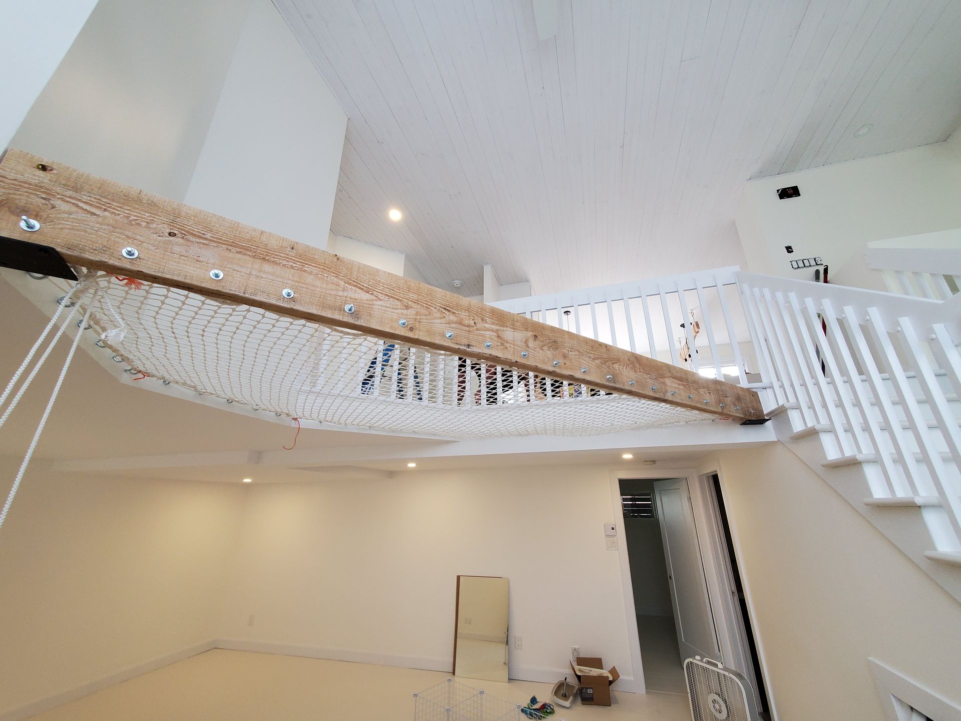 Une pièce avec un escalier et un hamac suspendu au plafond.