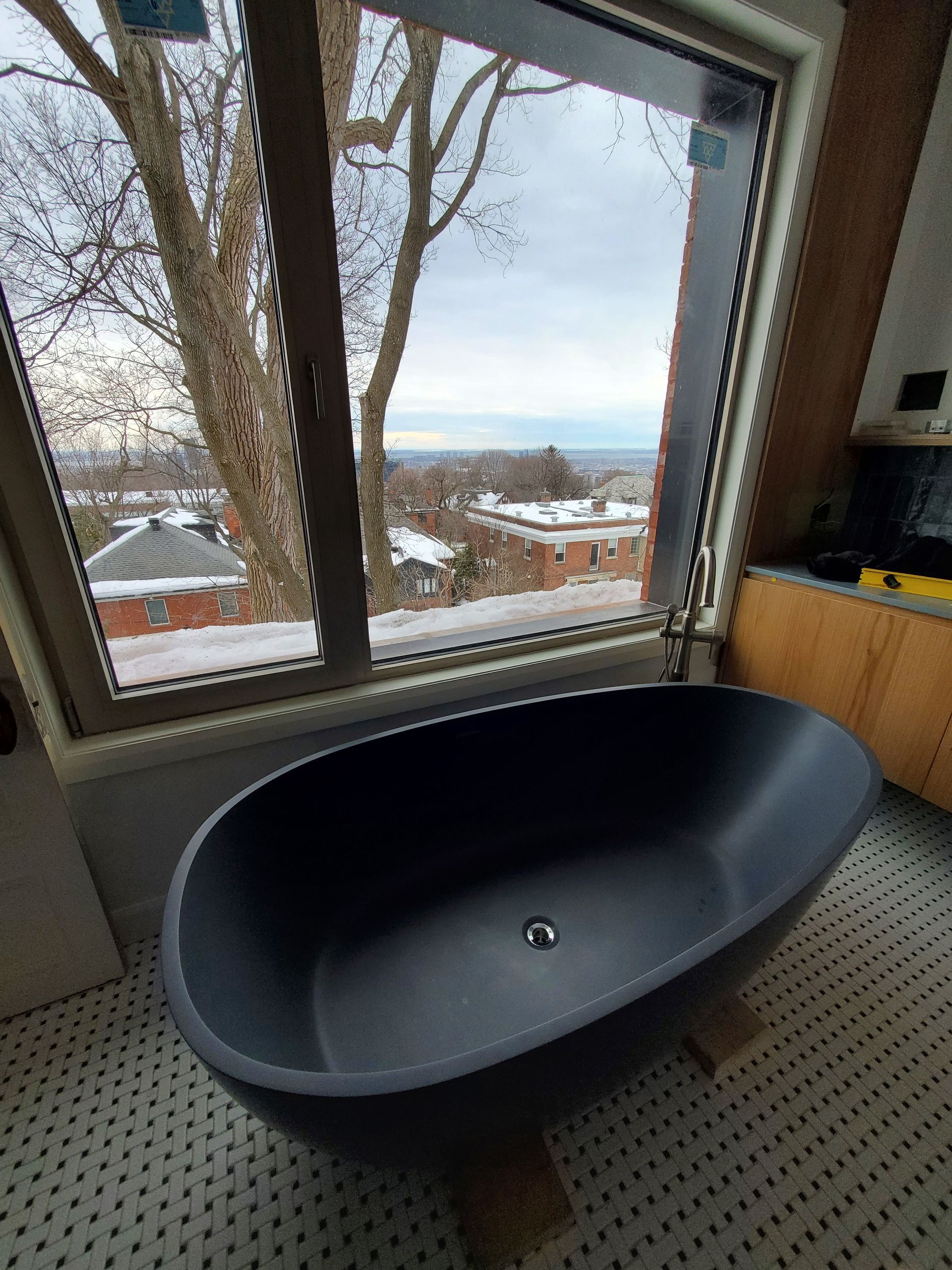 Une baignoire noire se trouve devant une grande fenêtre dans une salle de bain.