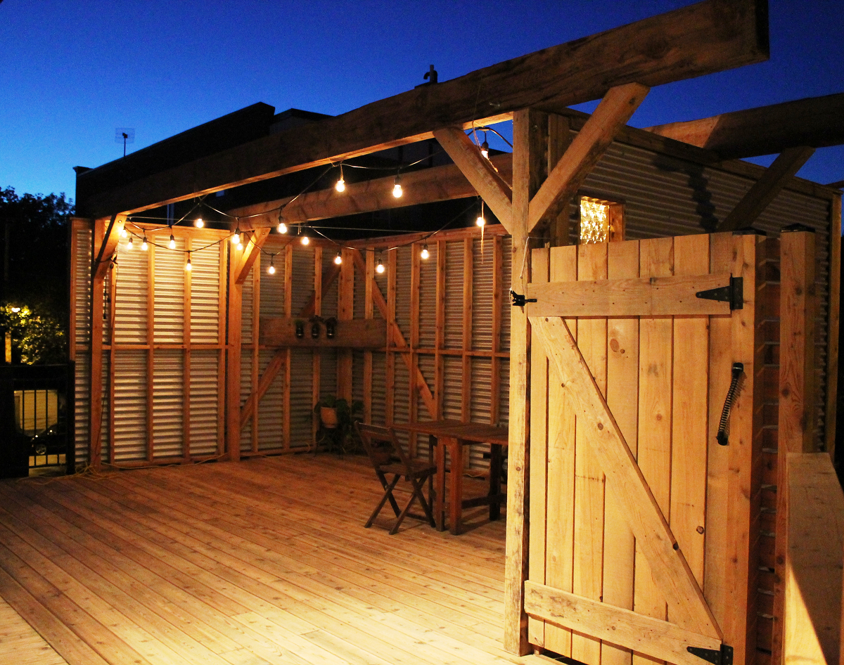 Une terrasse en bois avec une table et des chaises sous une pergola la nuit