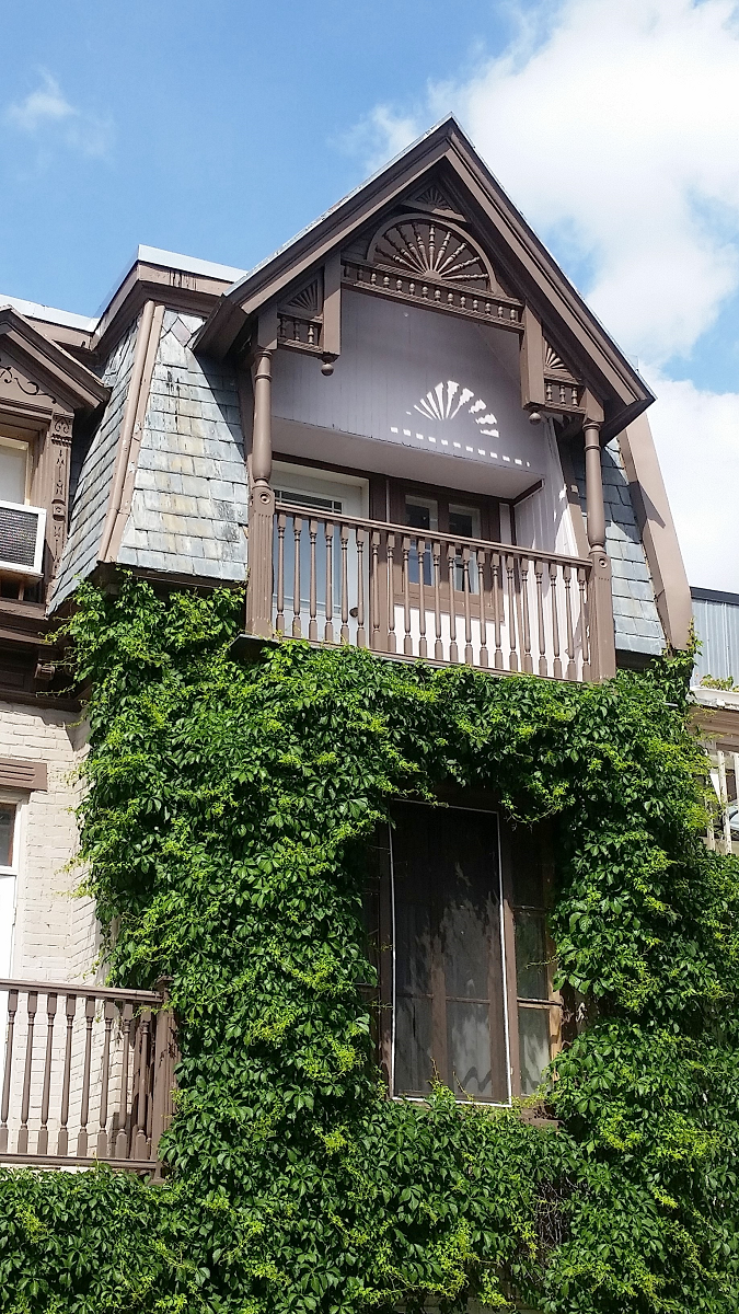 Une grande maison avec un balcon et du lierre poussant sur le côté.