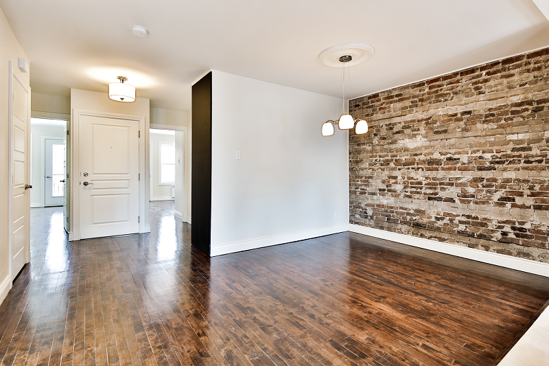 Une pièce vide avec du parquet et un mur de briques.