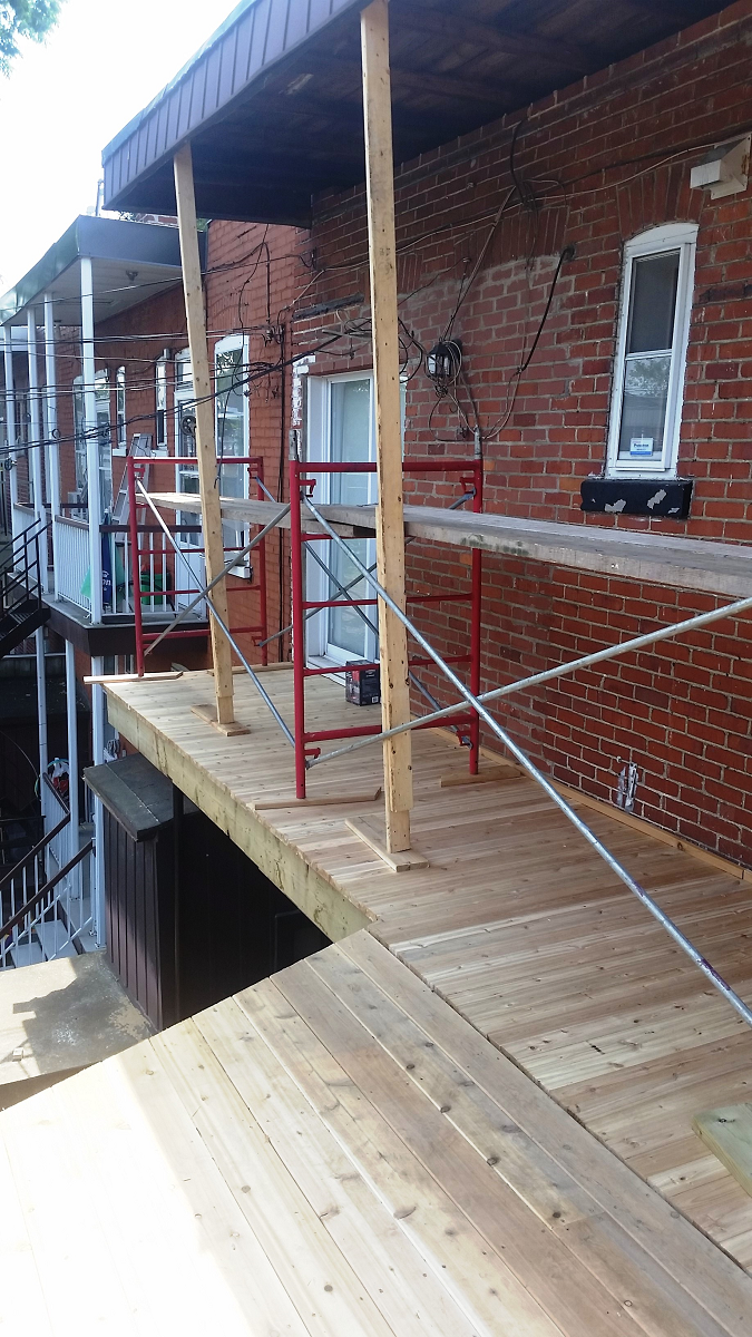 Une terrasse en bois est en cours de construction sur le côté d'un bâtiment en brique.