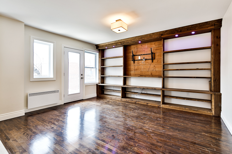 Un salon vide avec parquet et étagères.