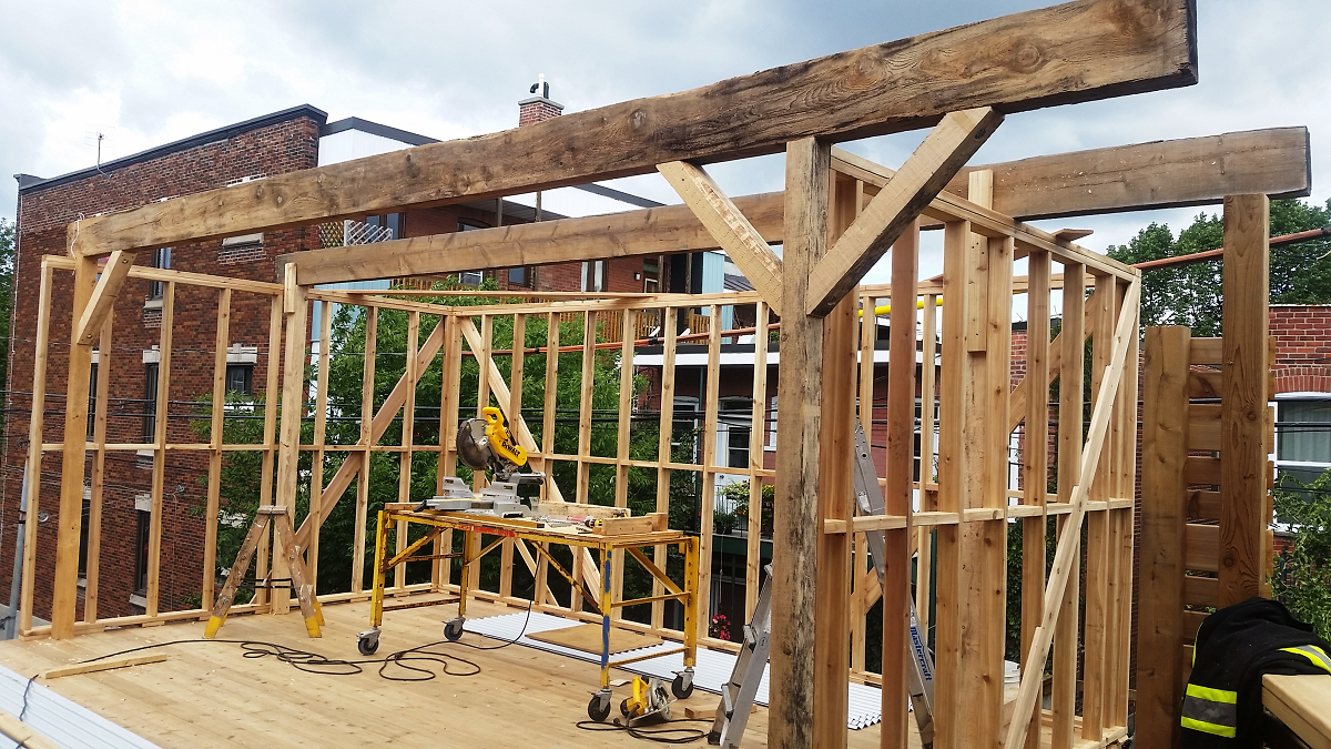 Une grande structure en bois est en cours de construction devant un bâtiment en brique.