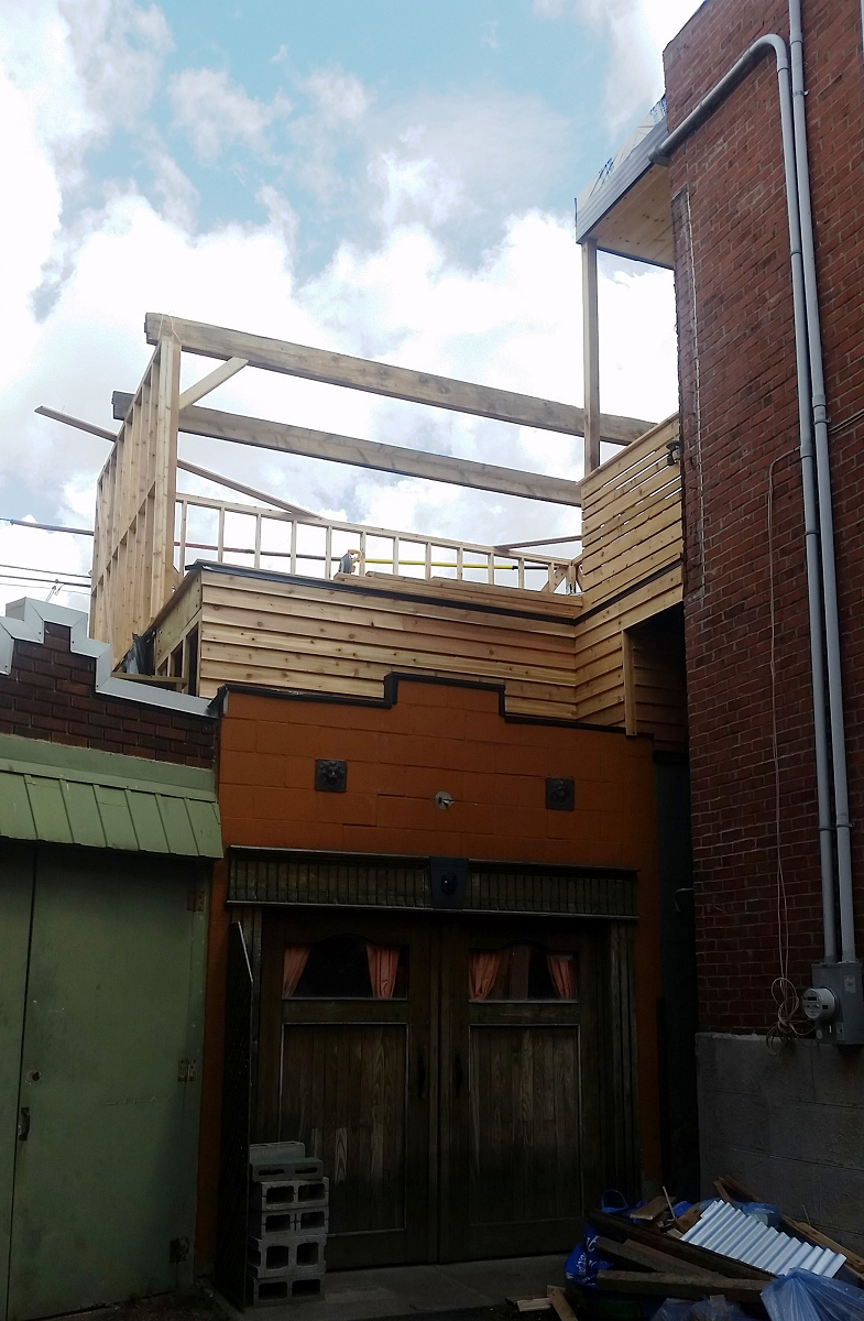 Une terrasse en bois est en cours de construction au sommet d'un bâtiment en brique.