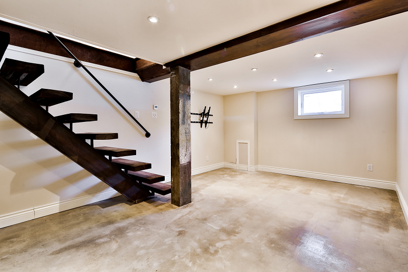 Un sous-sol vide avec un escalier en bois et un sol en béton.