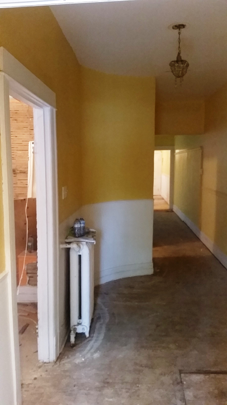 Un long couloir avec des murs jaunes et un radiateur au milieu.