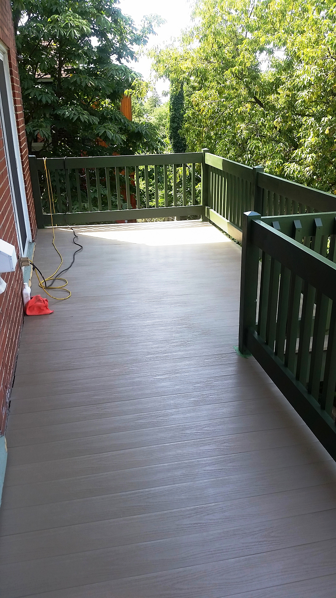 Une grande terrasse avec une balustrade verte et des arbres en arrière-plan.