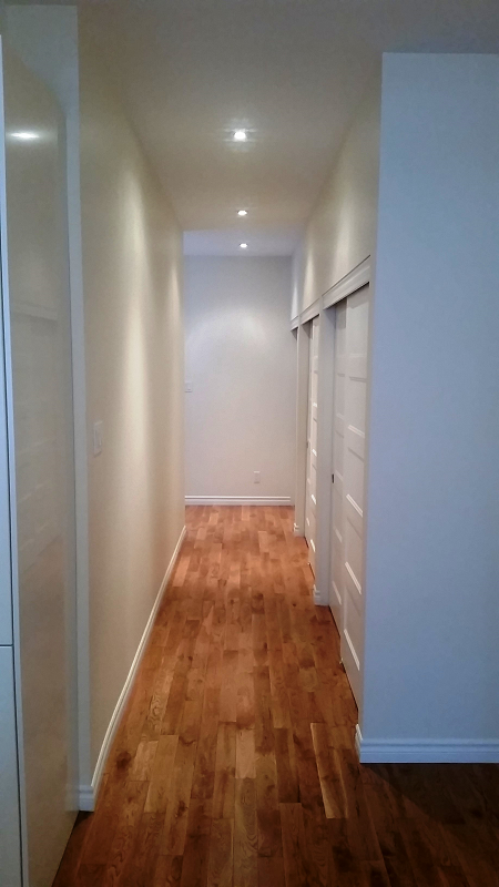 Un long couloir avec parquet et murs blancs.