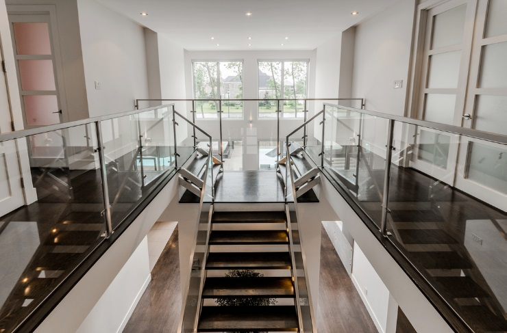 Un couloir avec des escaliers et une balustrade en verre dans une maison