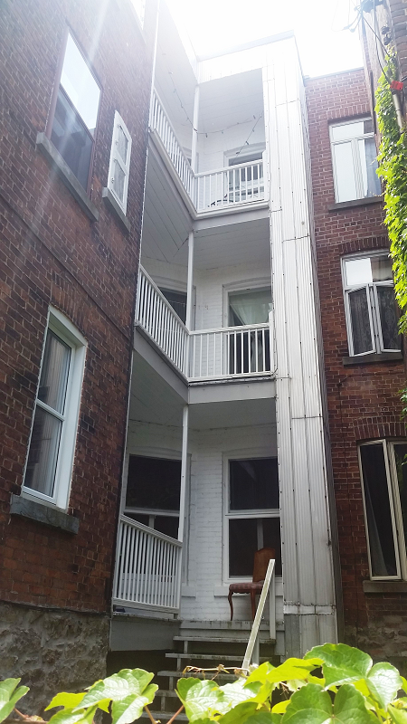 Un bâtiment en brique avec balcon et escalier entre deux autres bâtiments en brique.