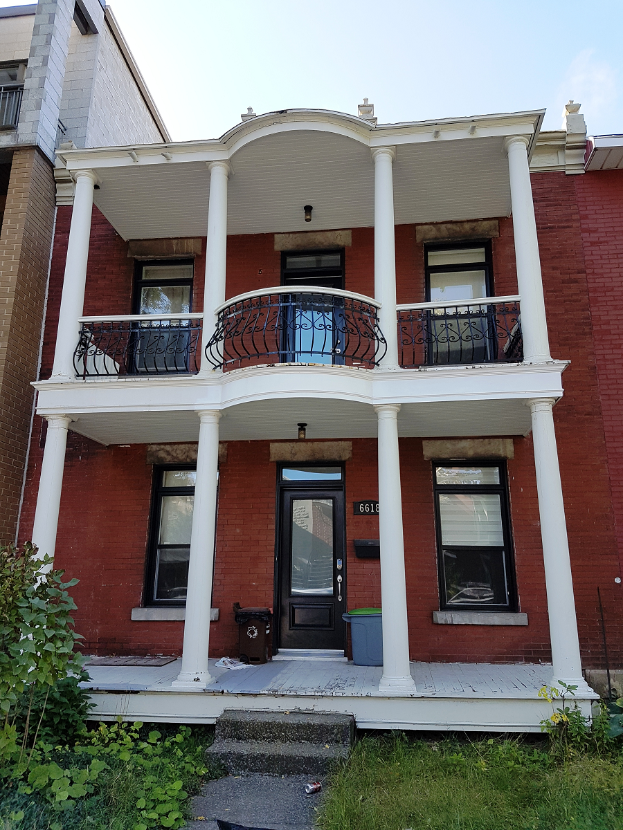 Une maison en briques rouges avec des colonnes blanches et un balcon.
