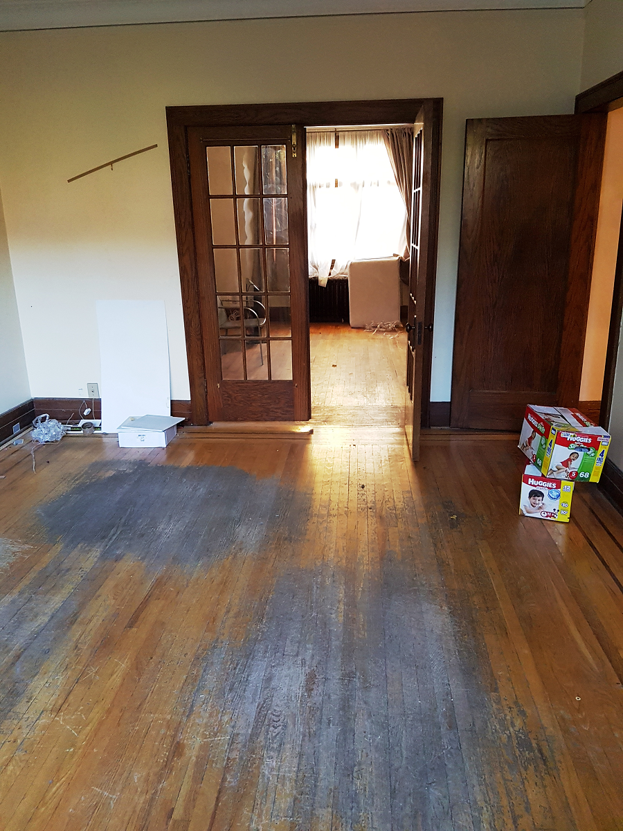 Un salon avec parquet et une pile de rouleaux de papier toilette au sol.