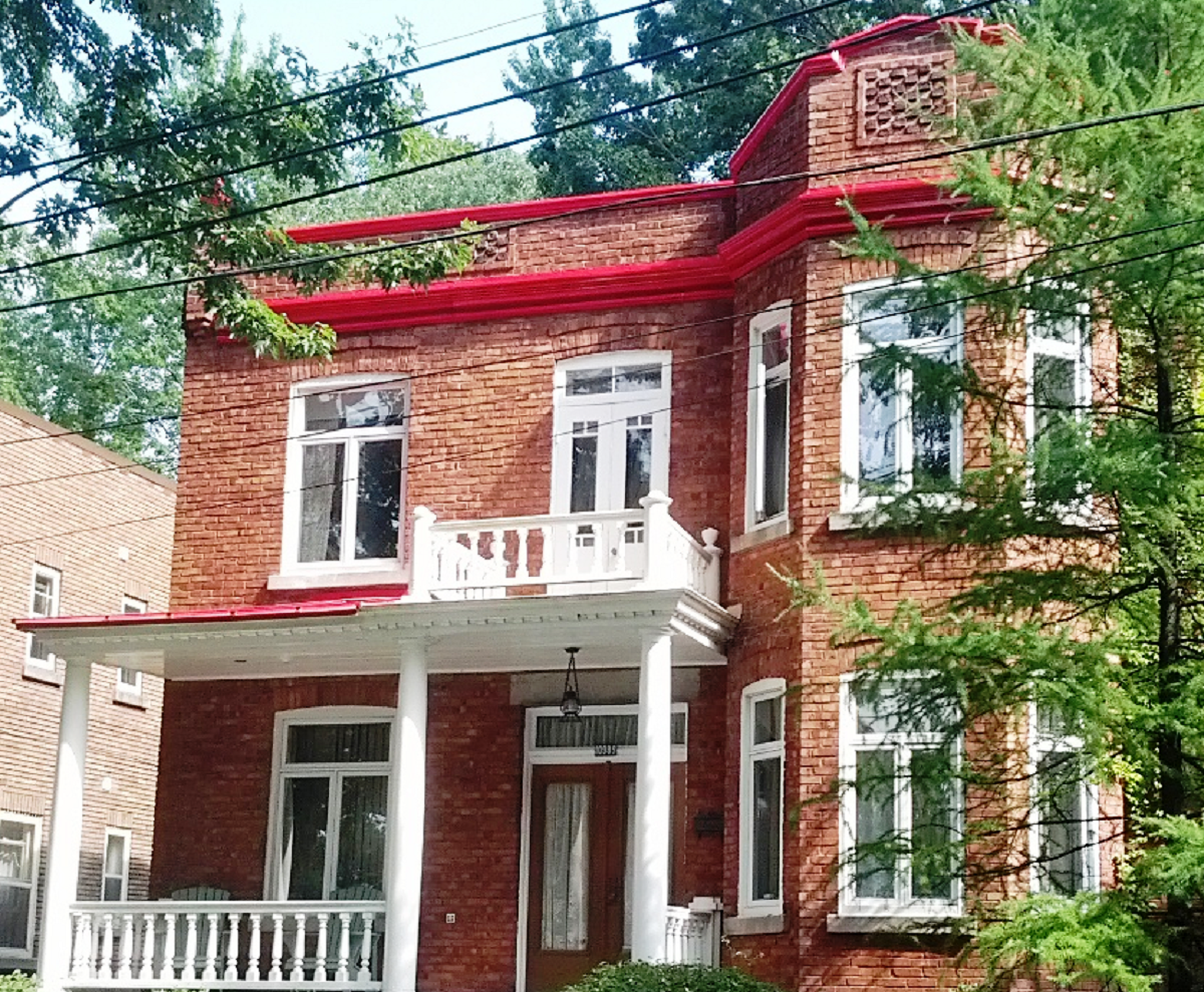 Une maison en brique avec un toit rouge et un porche blanc