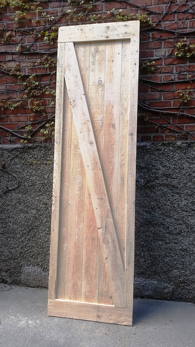 Une porte en bois se trouve sur le trottoir devant un mur de briques.