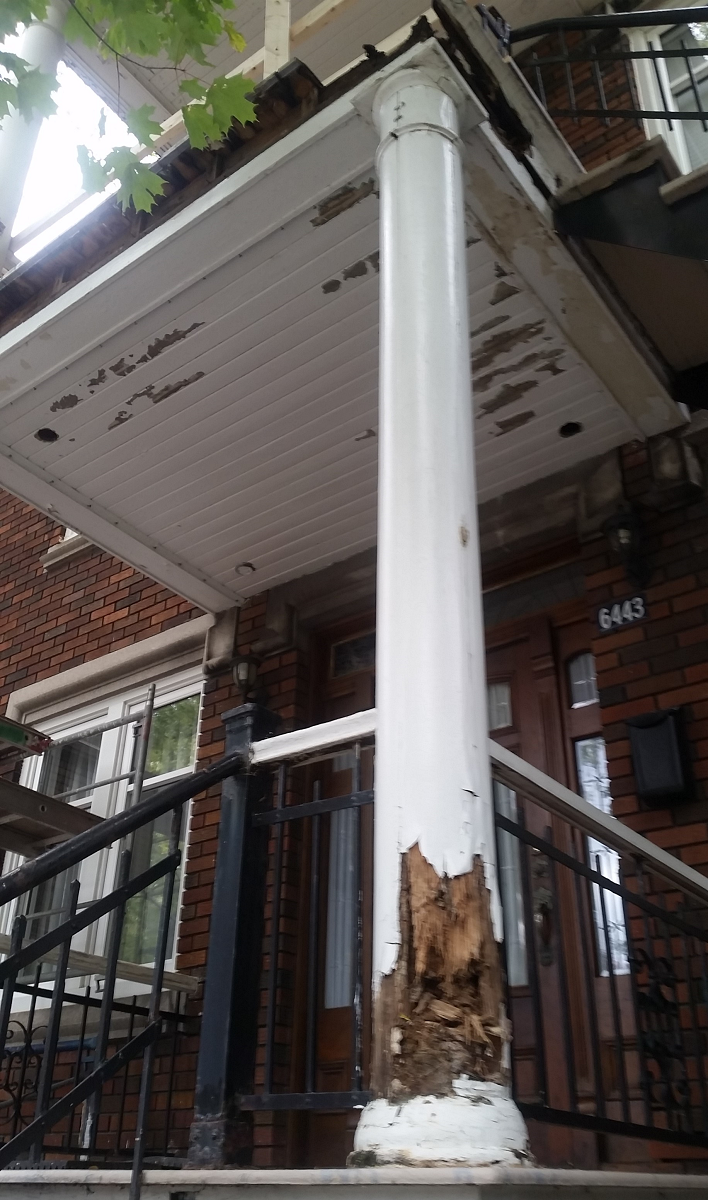 Un pilier blanc percé d'un trou se trouve devant un bâtiment en brique.