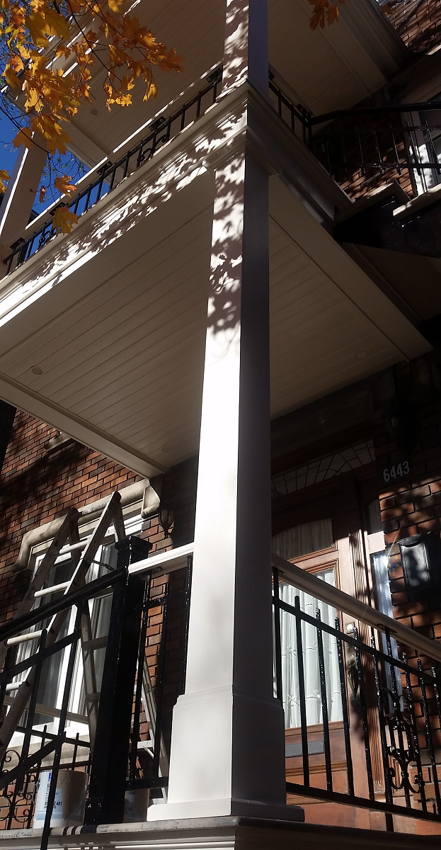 Un porche avec un pilier blanc et une balustrade noire.