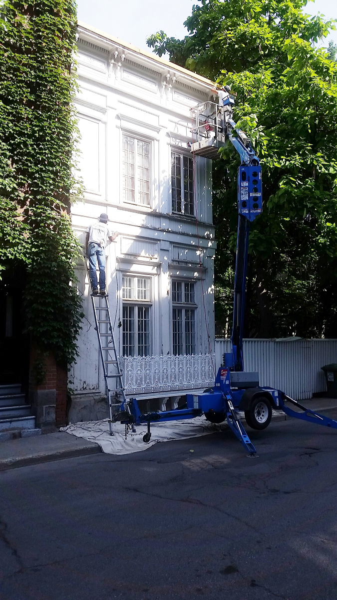 Une grue bleue est utilisée pour peindre un bâtiment blanc.
