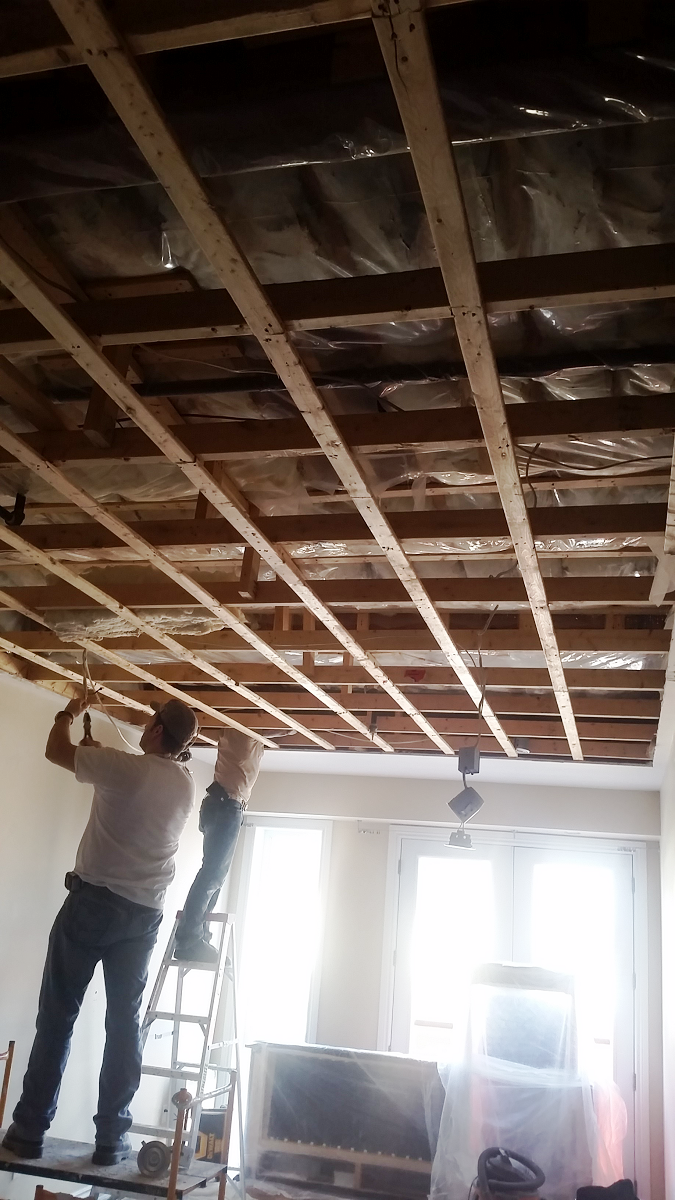 Deux hommes travaillent sur un plafond en bois dans un salon.