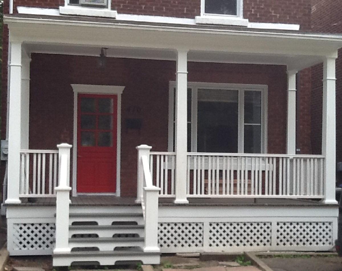Une maison en brique avec un porche blanc et une porte rouge