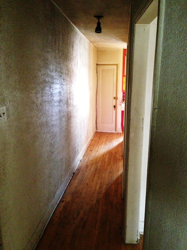 Un long couloir avec du parquet et une porte blanche