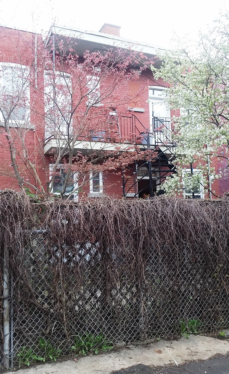 Un bâtiment en briques rouges avec un balcon et une clôture devant.