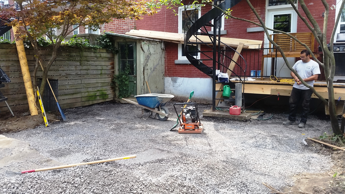 Un homme se tient dans une cour de gravier devant un bâtiment en brique.