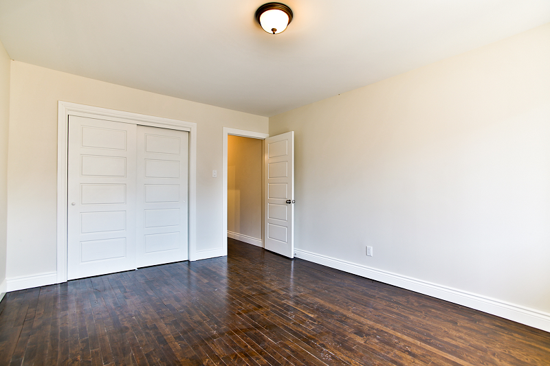 Une chambre vide avec parquet et murs blancs.