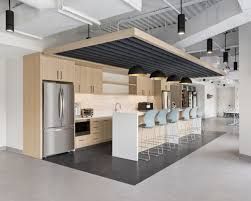 Modern office kitchen with light wood cabinets, stainless steel appliances, and a black and white island with bar seating.