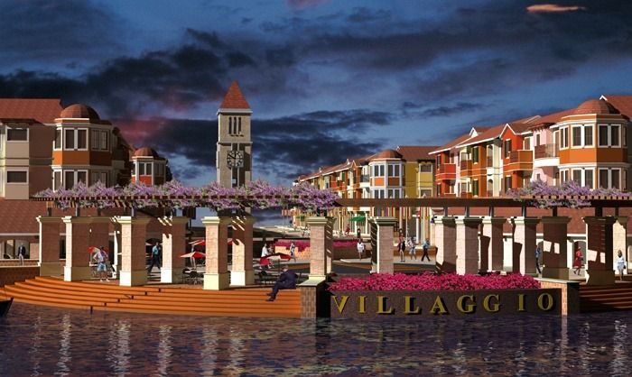 A waterfront view of Villaggio, an Italian-themed community. Buildings with colorful facades and a tall tower stand at dusk.