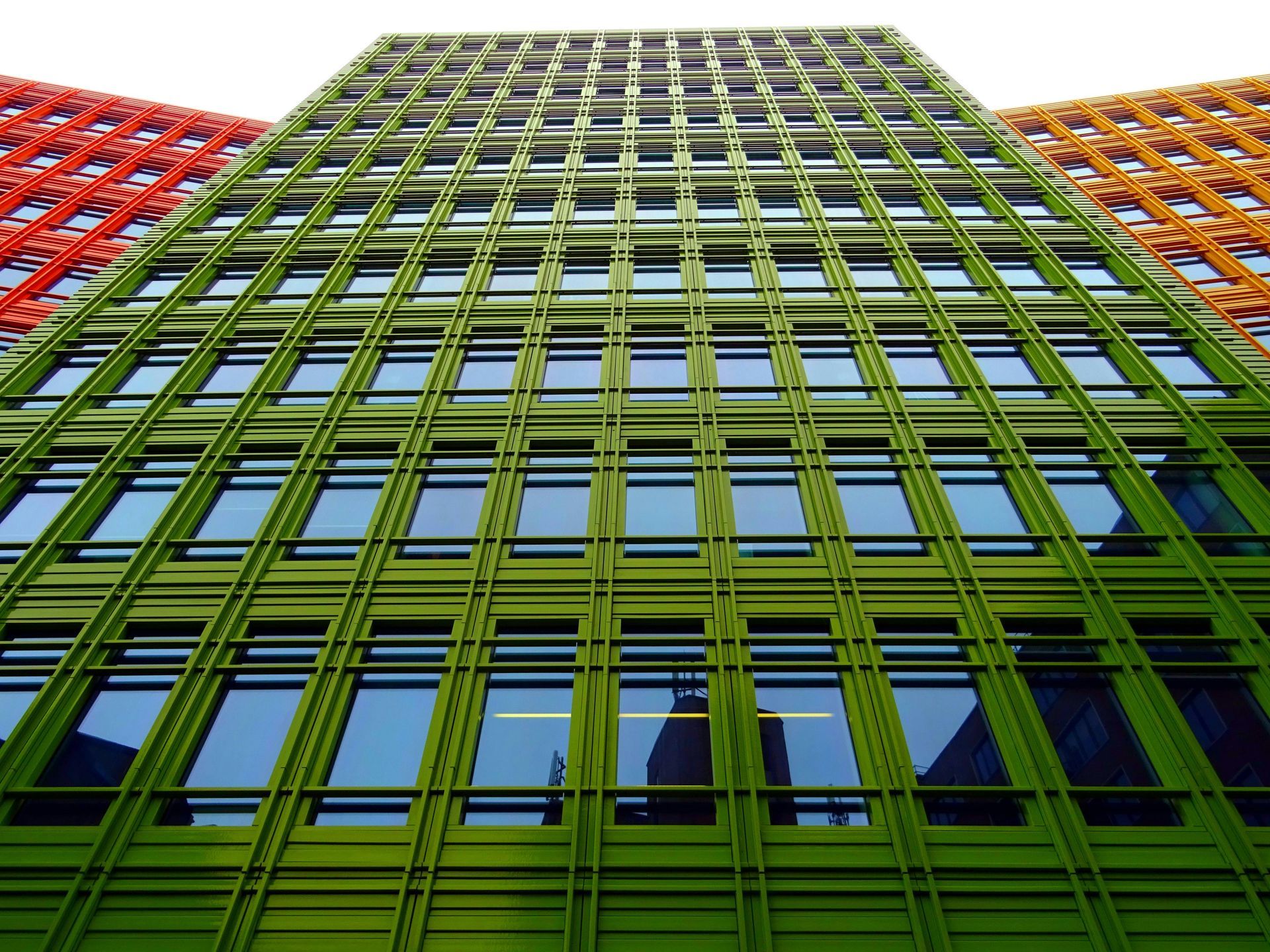 Green, orange, and red multi-story building facade with many windows, viewed from below.