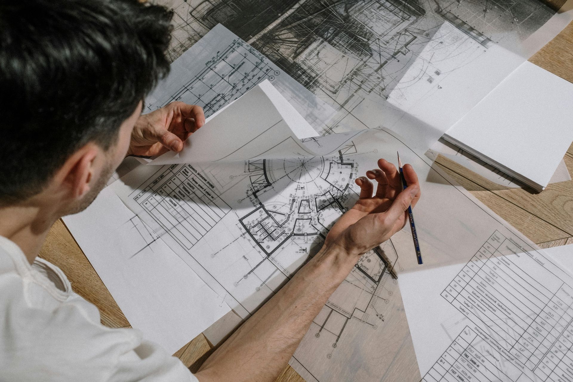 Person examining architectural blueprints with a pencil on a desk.