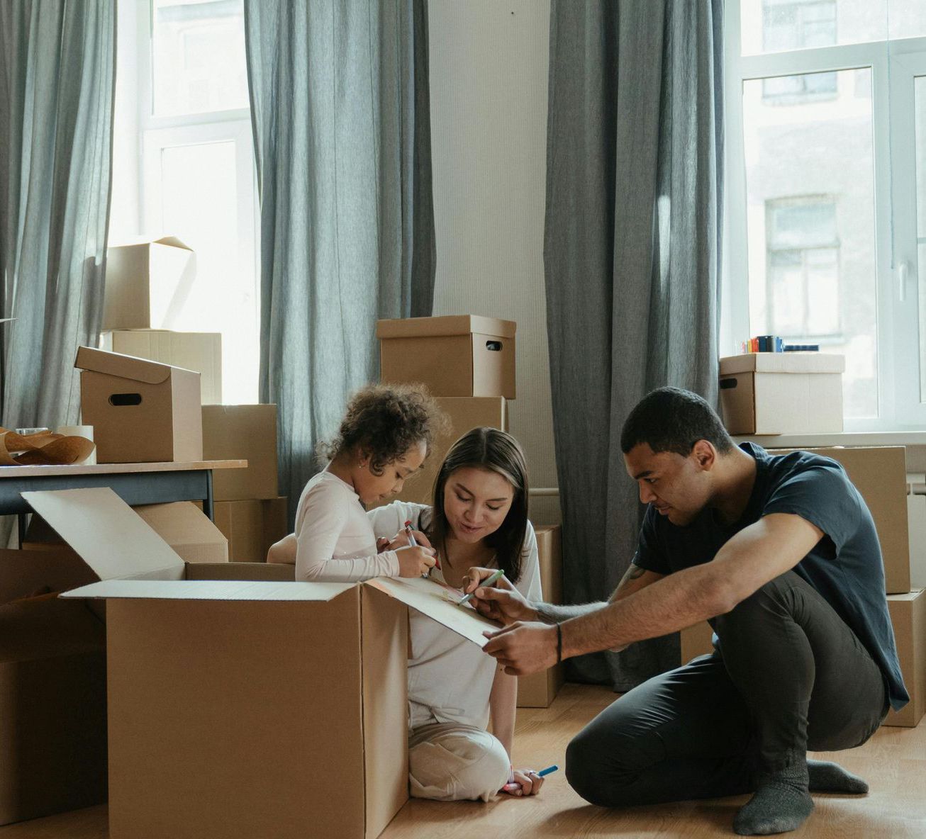 A man and a woman are kneeling on the floor in a room filled with cardboard boxes.