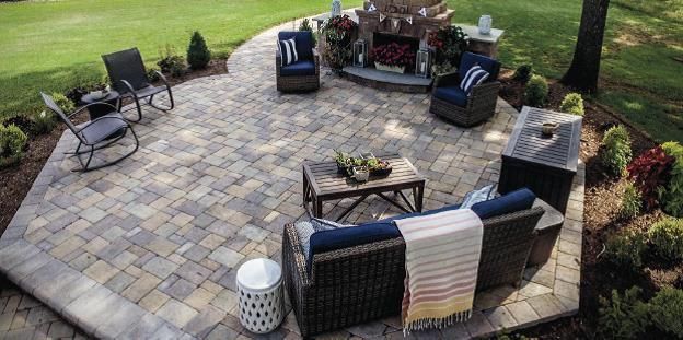 Outdoor patio with wicker seating, fire pit, and potted plants on a stone paver площадка