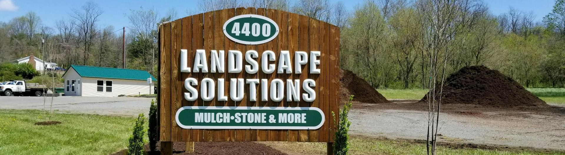 Landscape Solutions sign beside gravel piles in a rural roadside lot under a blue sky.