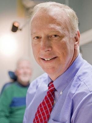 A man in a blue shirt and red tie is smiling for the camera.