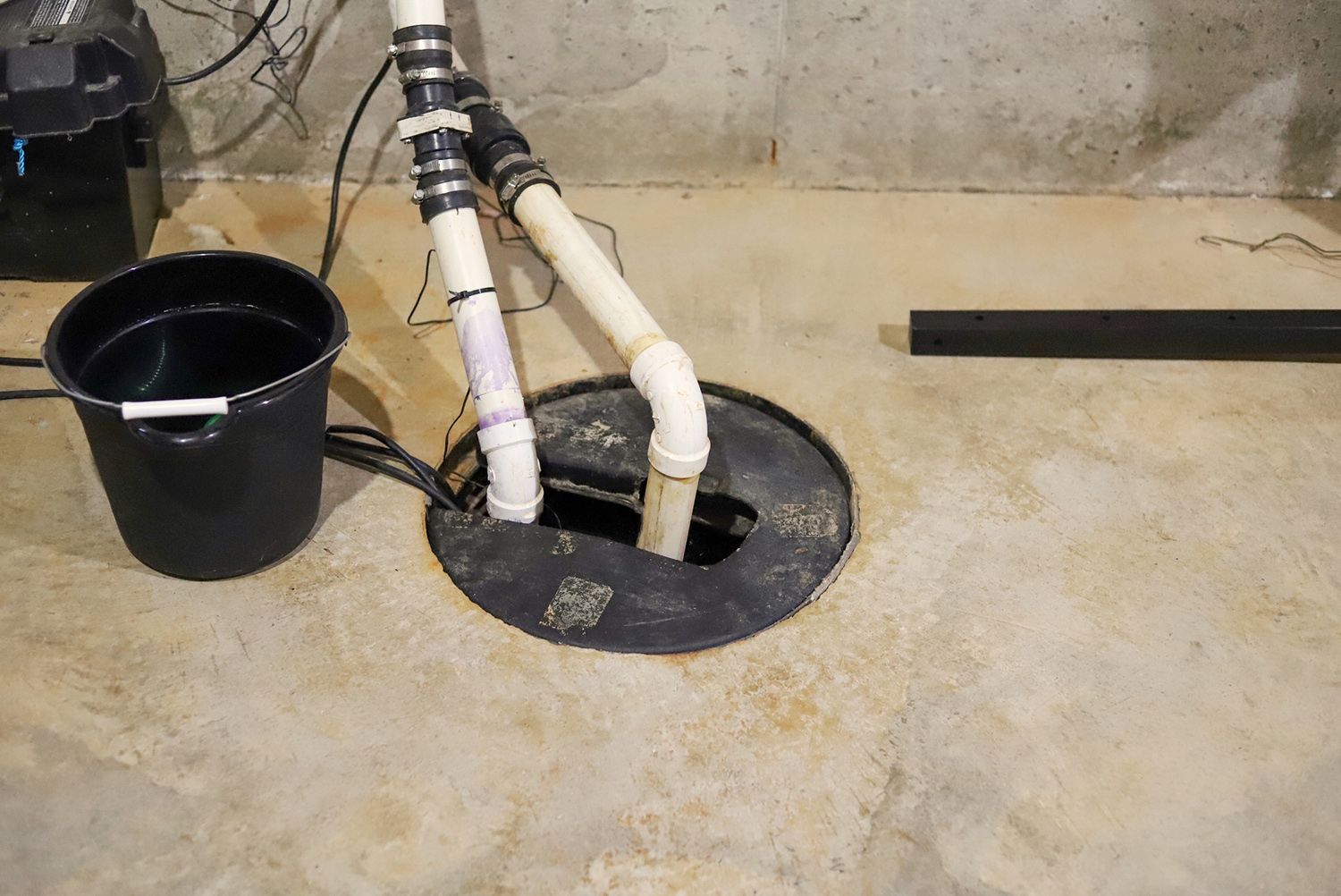 A bucket of water is sitting next to a sump pump in a basement.