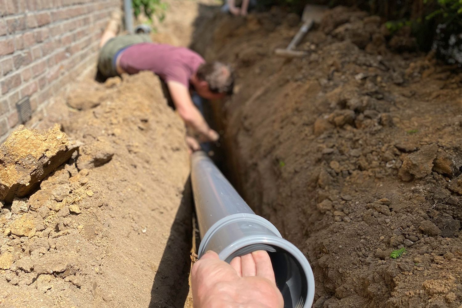 A man is digging a hole in the ground to install a pipe.