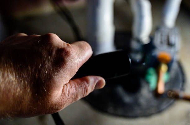 A person is holding a black object in their hand in front of a drain.