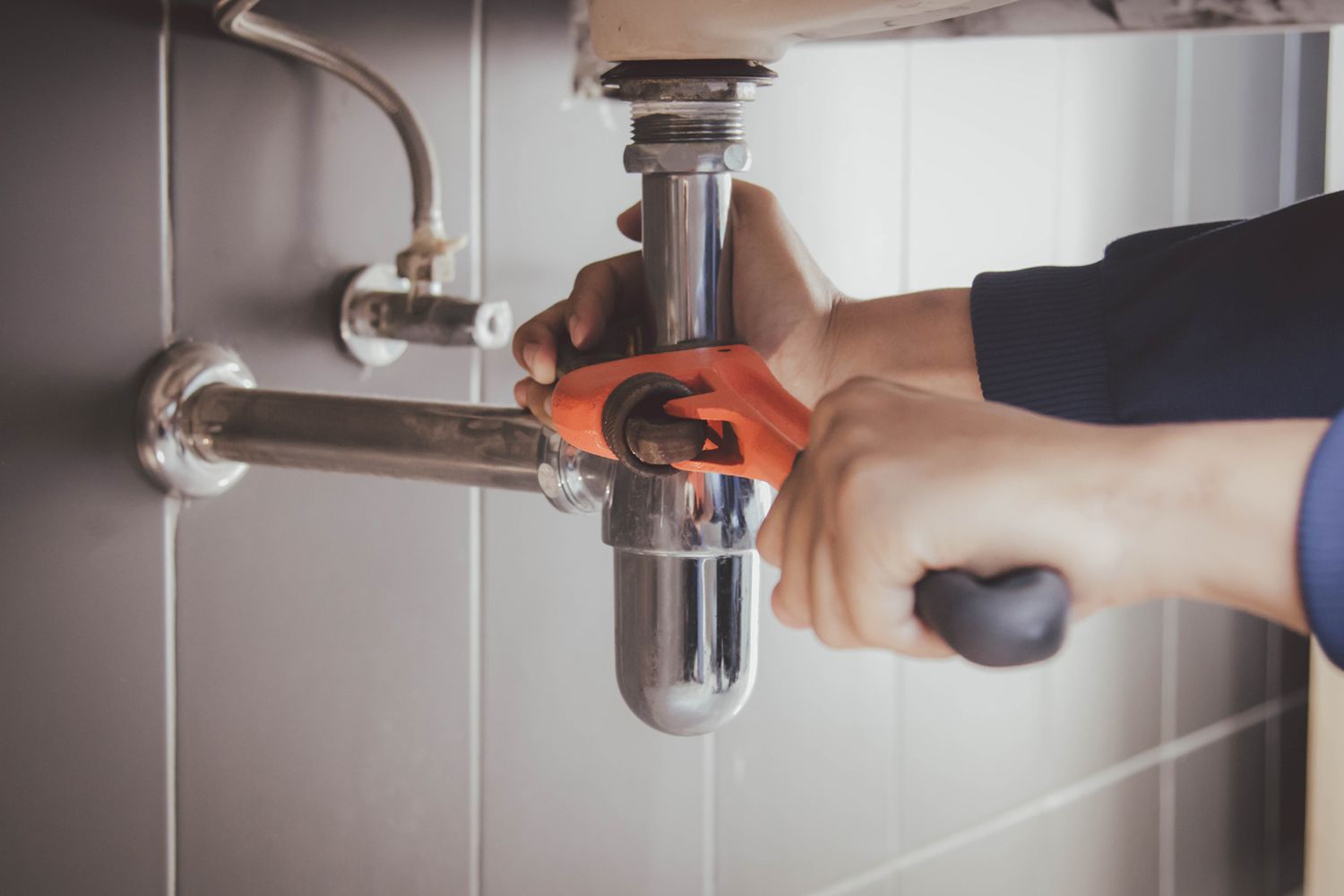A plumber is fixing a sink pipe with a wrench.