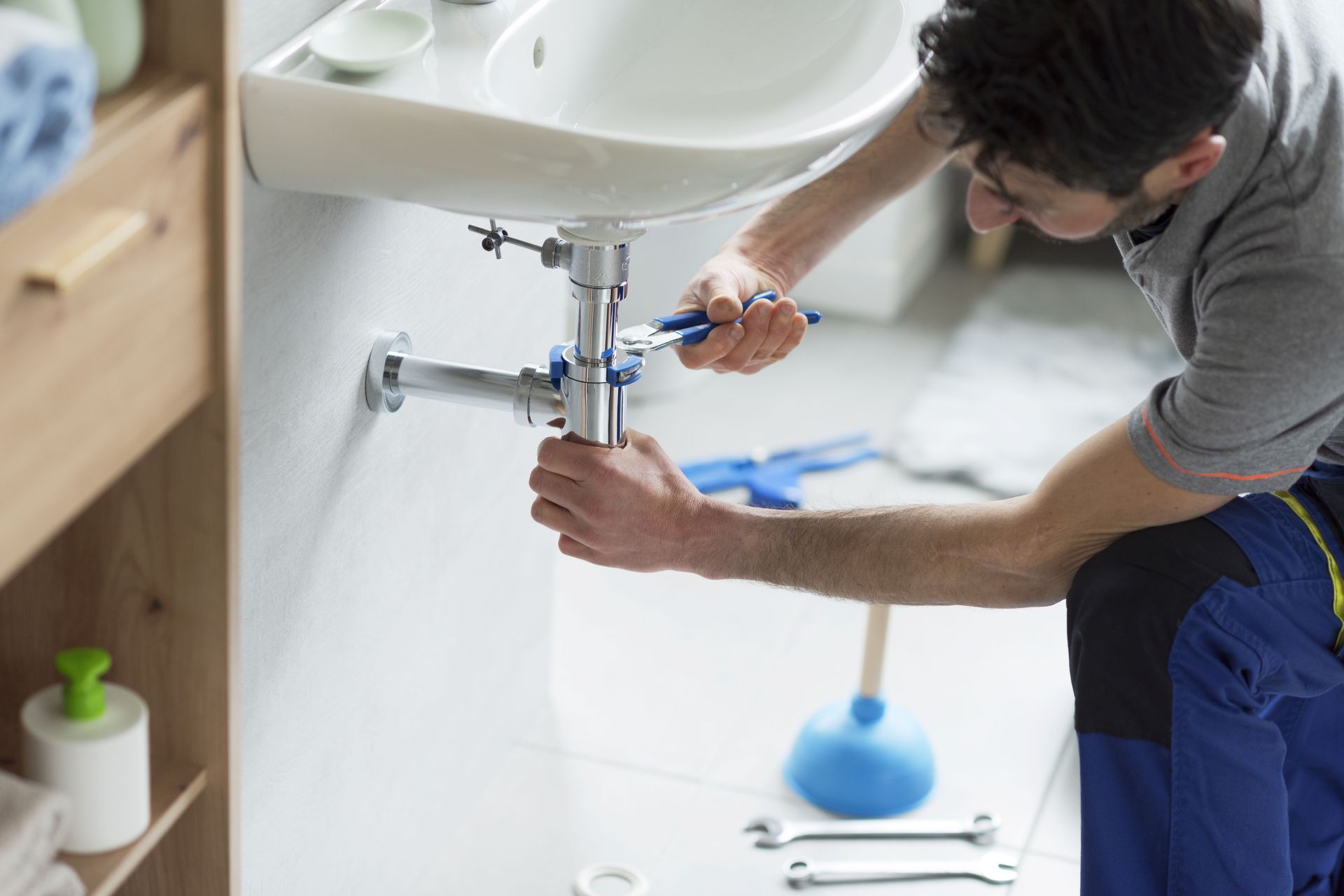 Plumber tightening pipes under bathroom sink.