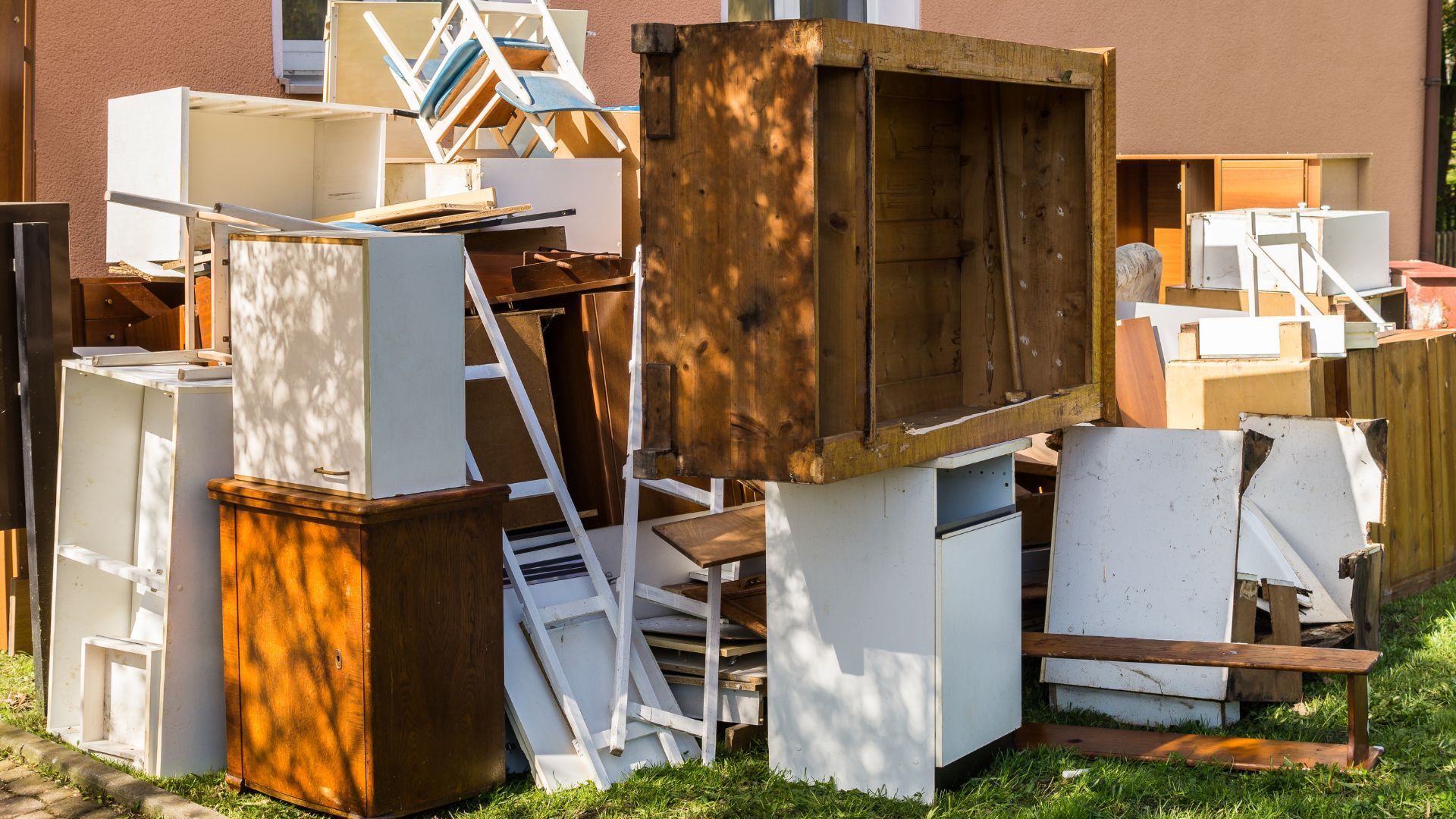 Pile of discarded wooden furniture and cabinets outside a building.