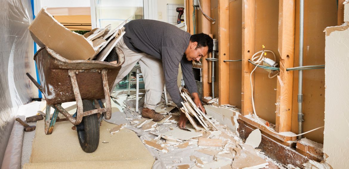 Man removing debris from a room under renovation, using a wheelbarrow.