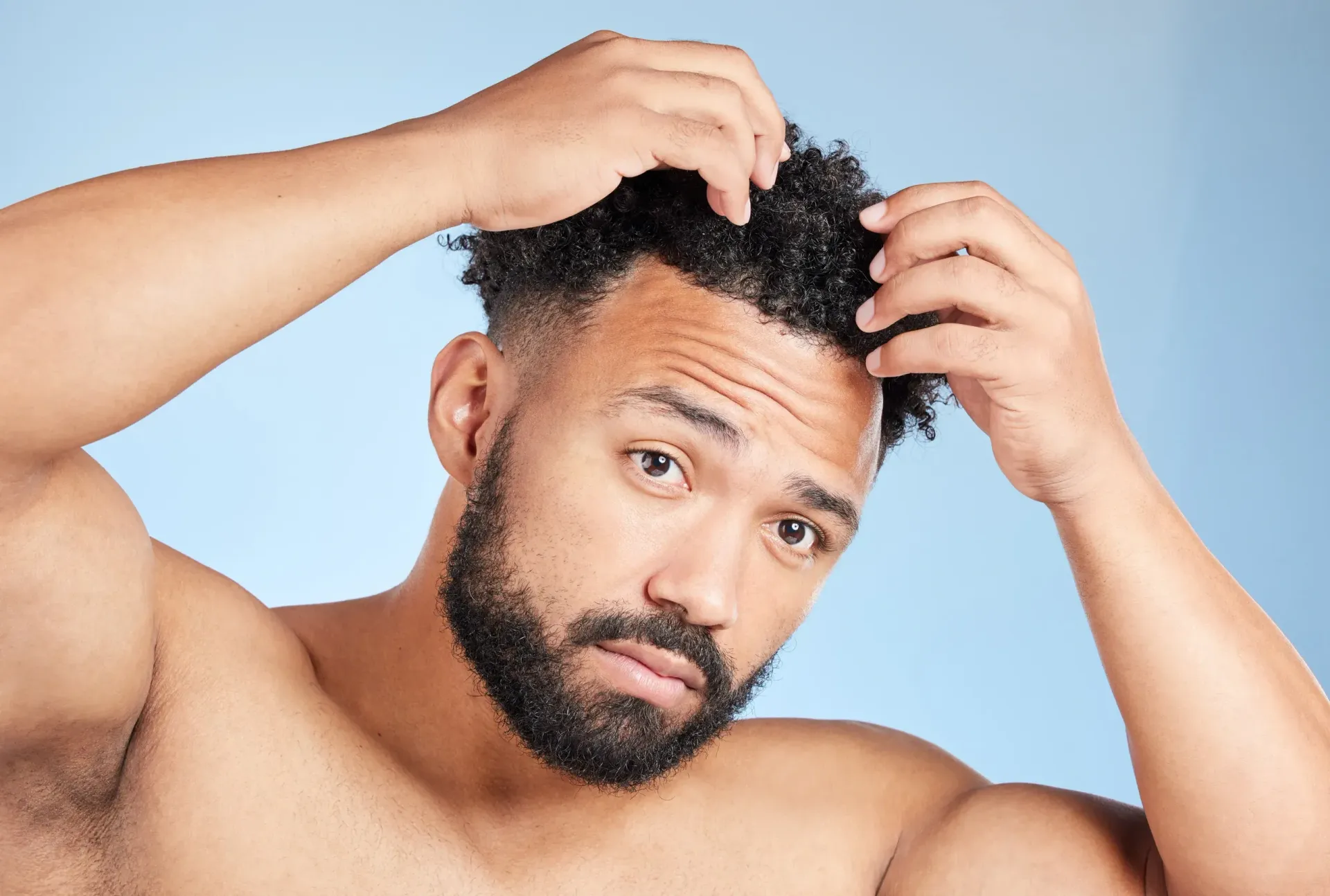 A shirtless man with a beard is looking at his hair.