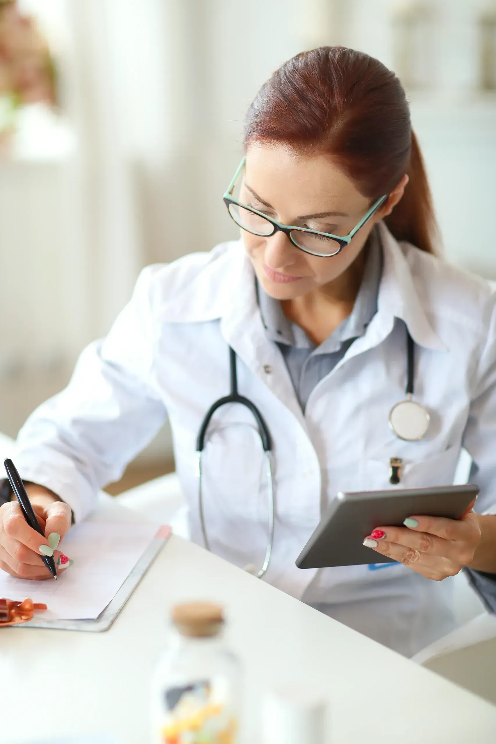 A female doctor is sitting at a desk using a tablet computer.