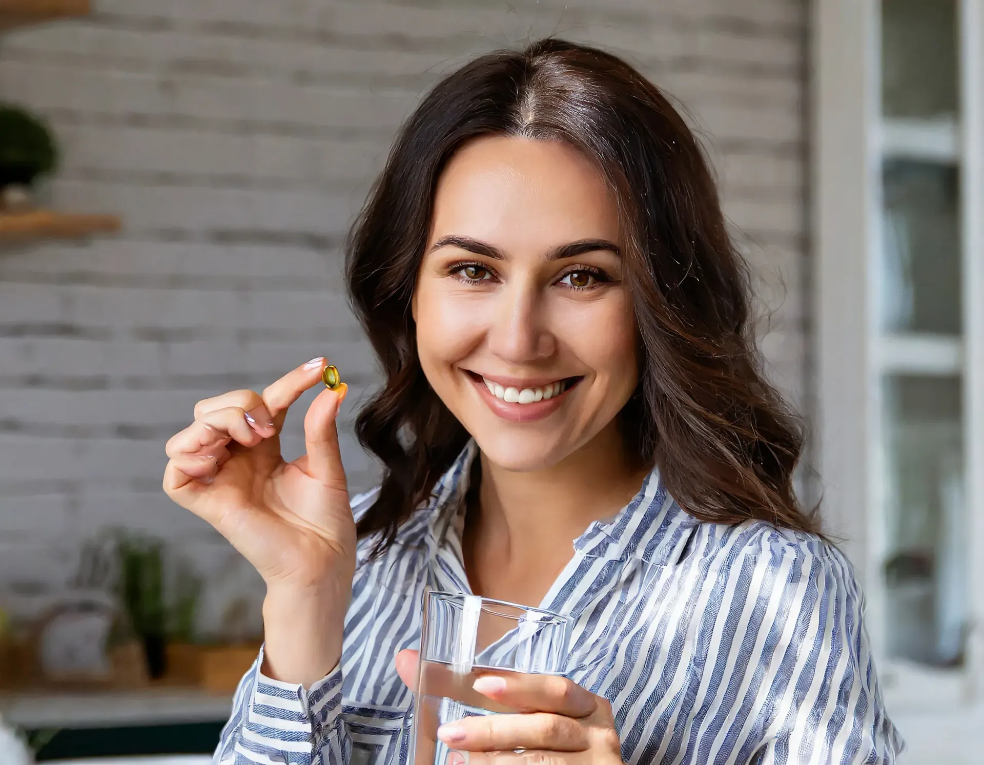 A woman is holding a pill and a glass of water.
