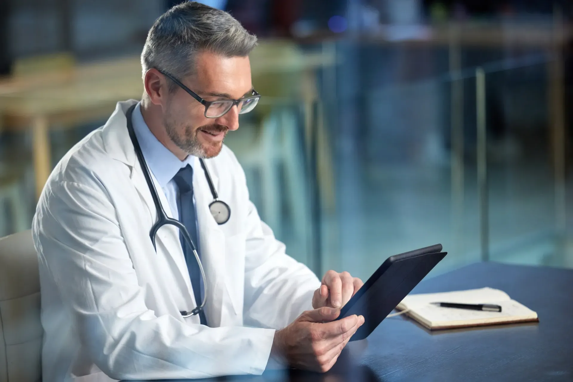 A doctor is sitting at a table using a tablet computer.