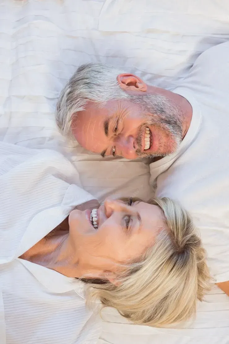 A man and a woman are laying on a bed and smiling.