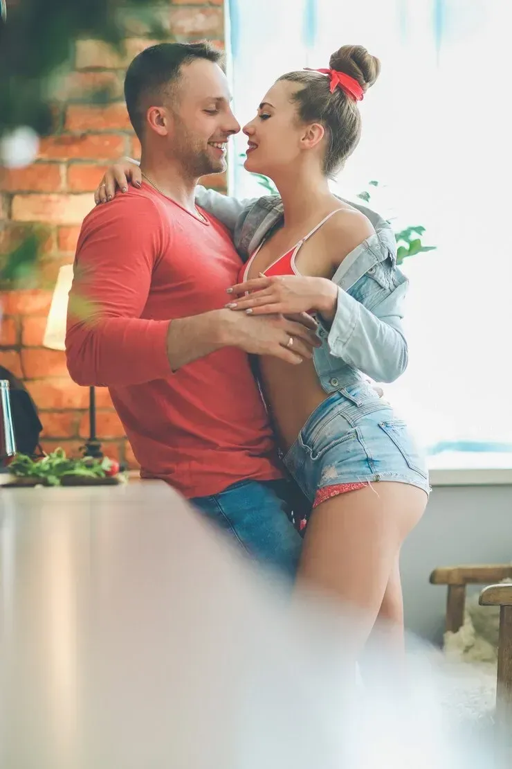 A man and a woman are hugging and kissing in a kitchen.