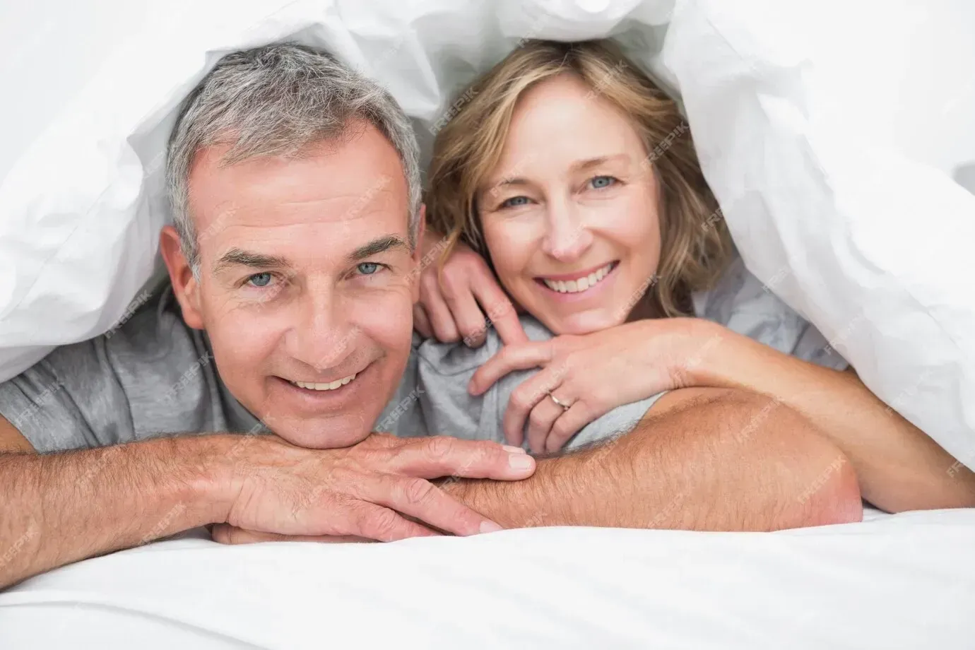 A man and a woman are laying under a blanket in bed.